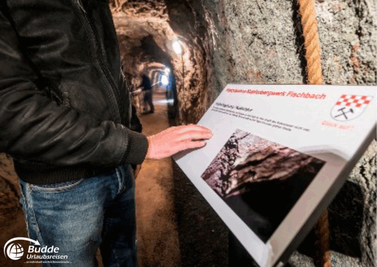 Urlaub Bad Kreuznach: Ein Besucher berührt ein Informationsschild im Kupferbergwerk Fischbach, umgeben von einem Tunnel. - buchbar im Reisebüro Budde Urlaubseisen