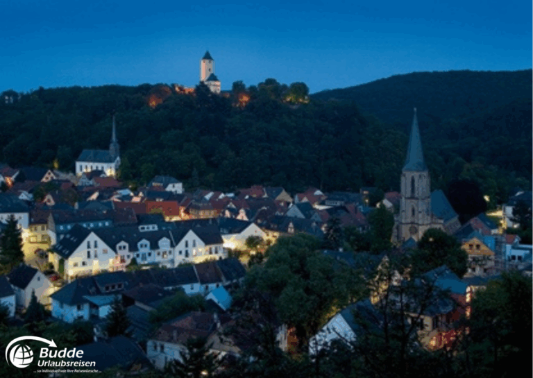 Urlaub an der Nahe: Nachtansicht von Bad Kreuznach mit beleuchteten Häusern und einem Hügel mit einem Turm. - buchbar im Reisebüro Budde Urlaubseisen
