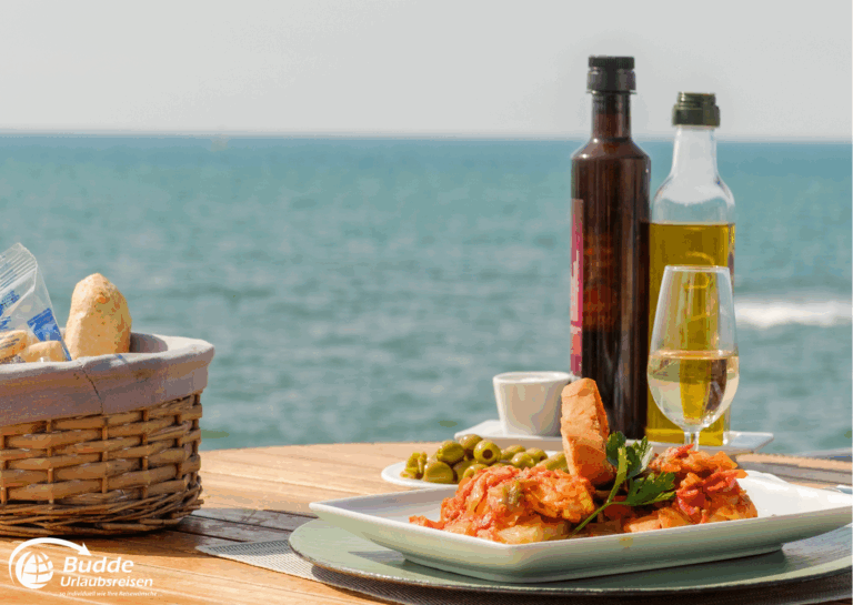 Mittelmeer per Schiff entdecken: Ein Teller mit Meeresfrüchten, Oliven, Öl und einem Glas Wein auf einem Tisch mit Meerblick. - buchbar im Reisebüro Budde Urlaubseisen