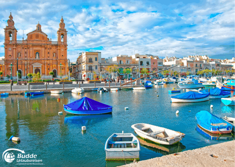 Mittelmeer per Schiff entdecken: Hafen in Malta mit mehreren Booten und einer Kirche im Hintergrund unter einem blauen Himmel. - buchbar im Reisebüro Budde Urlaubseisen