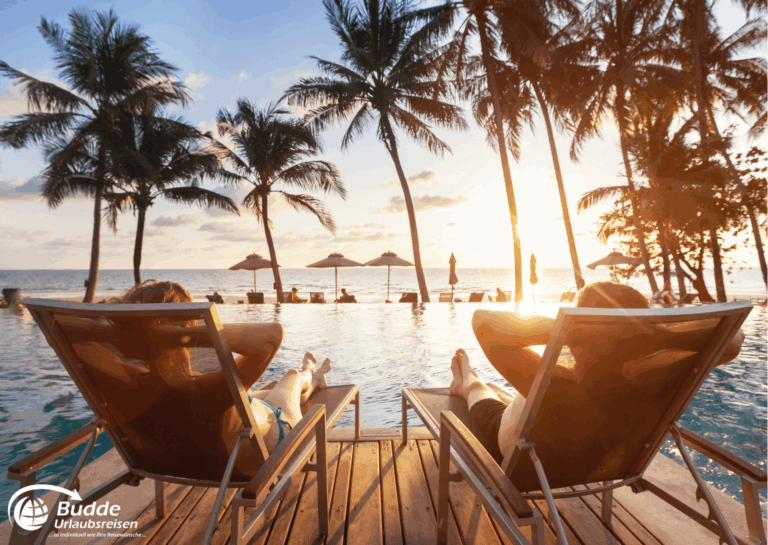 Romantikurlaub zu Zweit: Zwei Personen entspannen auf Liegen am Pool mit Blick auf den Sonnenuntergang und Palmen. - buchbar im Reisebüro Budde Urlaubseisen