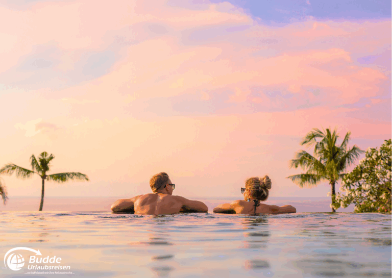 Romantikurlaub zu Zweit: Ein Paar entspannt im Infinity-Pool mit Blick auf den Sonnenuntergang und Palmen im Hintergrund. - buchbar im Reisebüro Budde Urlaubseisen