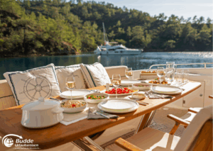 Romantikurlaub zu Zweit: Ein gedeckter Tisch auf einer Yacht mit verschiedenen Speisen und Getränken, umgeben von Wasser. - buchbar im Reisebüro Budde Urlaubseisen