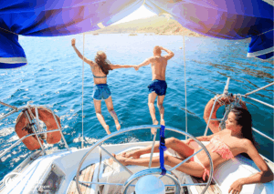 Romantikurlaub zu Zweit: Zwei Personen springen von einer Yacht ins Wasser, während eine dritte Person auf dem Deck sitzt. - buchbar im Reisebüro Budde Urlaubseisen