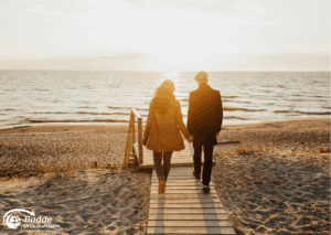 Romantikurlaub zu Zweit: Ein Paar hält Händchen und geht einen Holzsteg entlang zum Strand bei Sonnenuntergang. - buchbar im Reisebüro Budde Urlaubseisen
