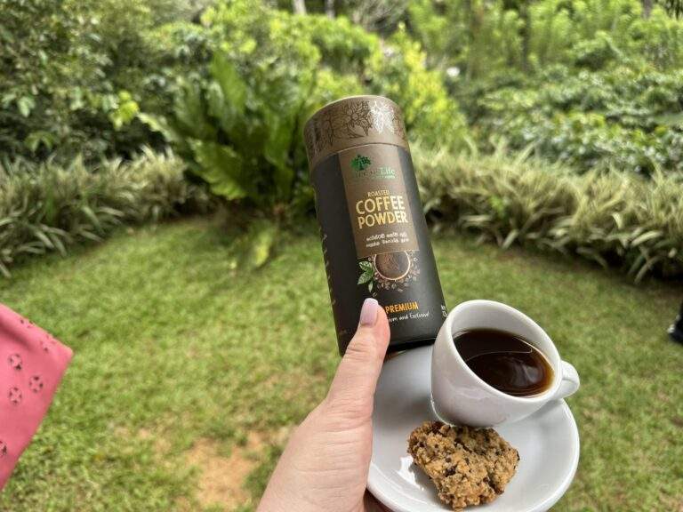 Kaffeeplantage in Kandy: Eine Hand hält eine Dose Kaffeepulver und eine Tasse Kaffee auf einem Teller mit einem Keks. - buchbar im Reisebüro Budde Urlaubseisen