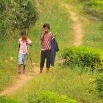 Zwei Kinder, eines mit einem Stock, gehen auf einem Weg durch eine grüne Landschaft in Sri Lanka. - Sri Lanka Urlaub buchen