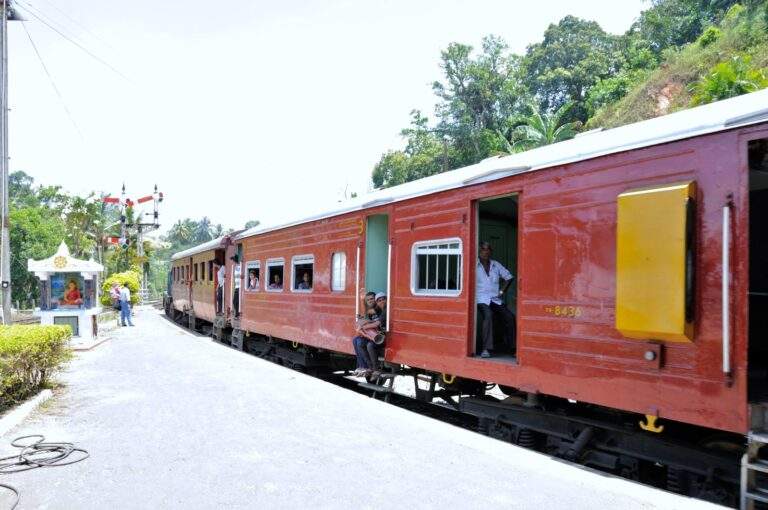 Ein roter Zug mit offenen Fenstern, der an einem Bahngleis in Sri Lanka hält. - Sri Lanka Urlaub buchen