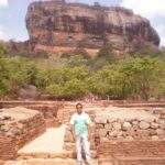 Mann steht vor dem Sigiriya-Felsen in Sri Lanka, umgeben von historischen Ruinen und Vegetation. - Sri Lanka Urlaub buchen