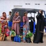 Vier Frauen in traditioneller Kleidung stehen neben einem blauen Tuk-Tuk und halten Einkaufstaschen mit Gemüse und Pflanzen. - Sri Lanka Urlaub buchen