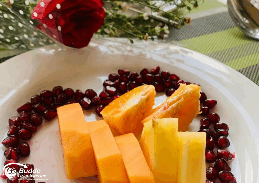 Ein Obstteller mit geschnittenen Melonenstücken und Granatapfelkernen auf einem weißen Teller. - buchbar im Reisebüro Budde Urlaubseisen