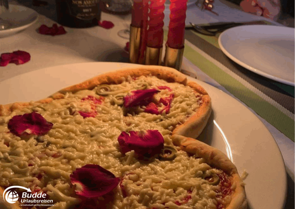 Praana Ayurvedic Boutique Hotel: Zwei Pizzastücke mit Käse und Oliven, dekoriert mit Rosenblättern auf einem Teller. - buchbar im Reisebüro Budde Urlaubseisen