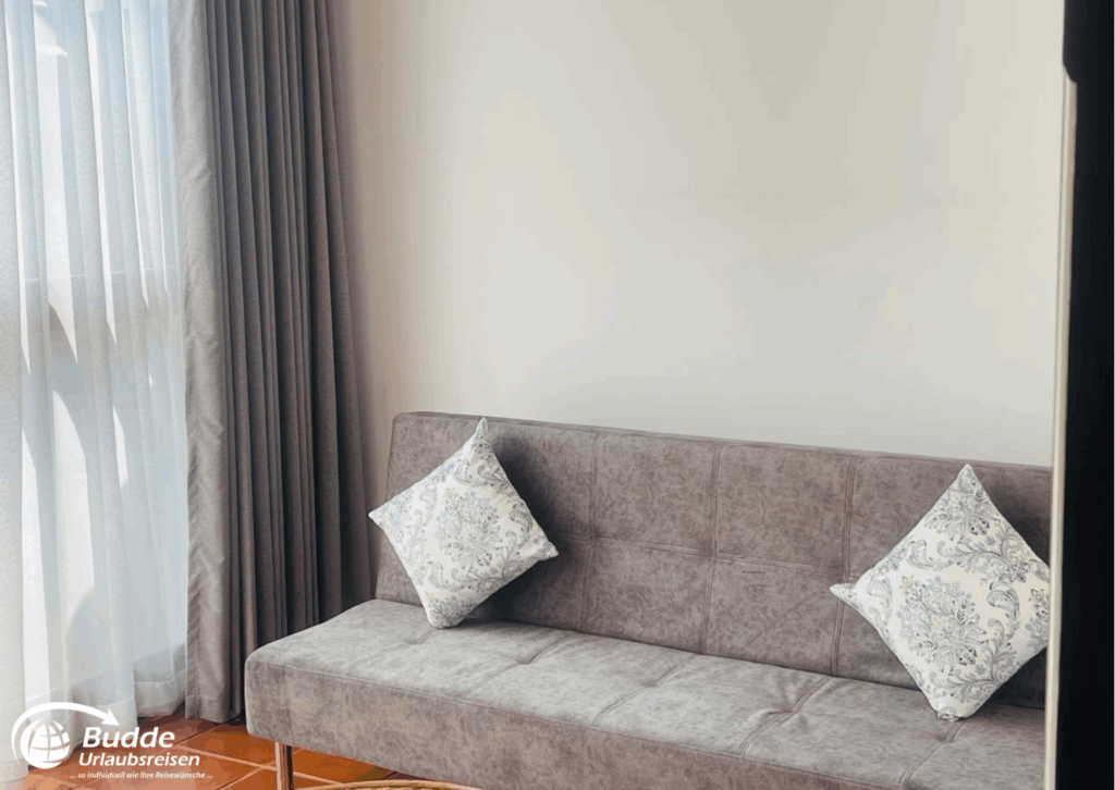 Grau gefärbtes Sofa mit zwei dekorativen Kissen in einem hellen Raum. - buchbar im Reisebüro Budde Urlaubseisen