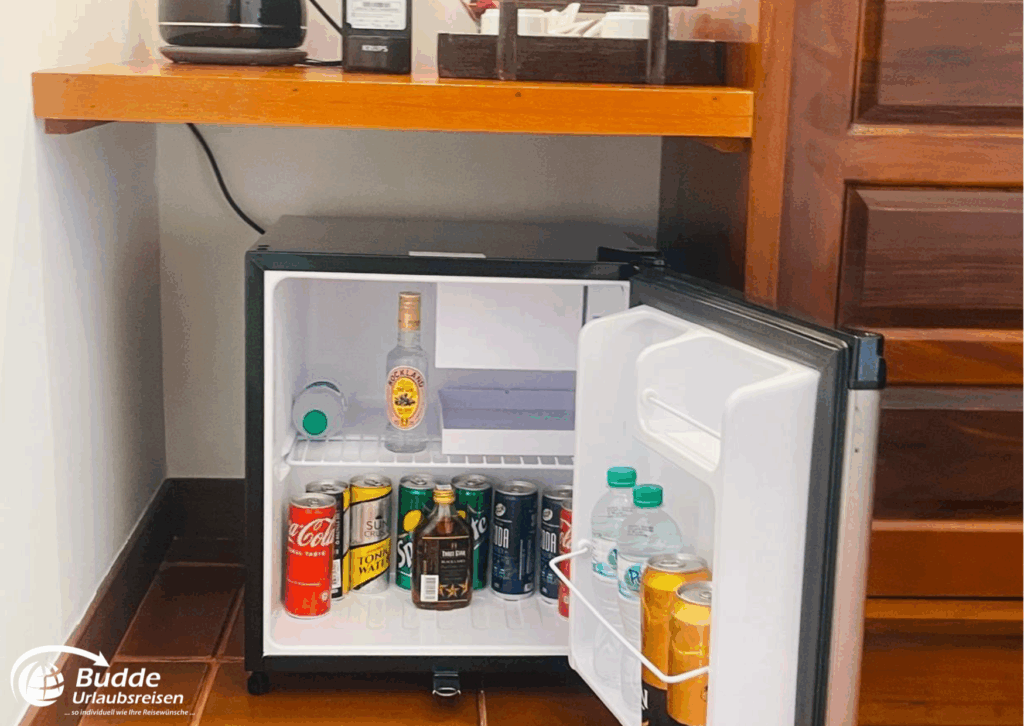 Offene Minibar mit verschiedenen Getränkedosen und Flaschen in einem Hotelzimmer. - buchbar im Reisebüro Budde Urlaubseisen