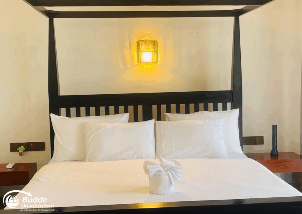 Ein Doppelbett mit weißen Kissen und einer dekorativen Handtuchfigur im Praana Ayurveda Boutique Hotel. - buchbar im Reisebüro Budde Urlaubseisen
