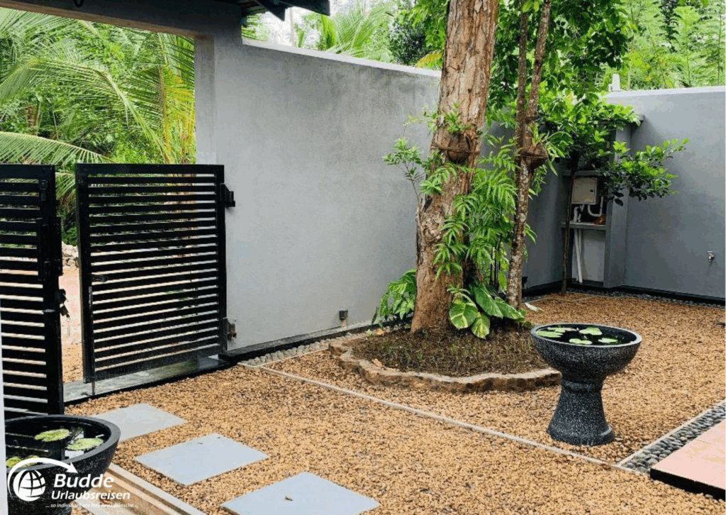 Eingangsbereich mit einem Baum, einem Wasserbecken und Kiesboden in einem Garten. - buchbar im Reisebüro Budde Urlaubseisen
