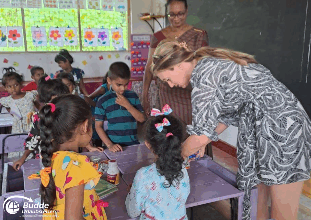 Lehrerin hilft Kindern beim Basteln in einem Klassenzimmer mit bunten Wänden und Tischen. - buchbar im Reisebüro Budde Urlaubseisen
