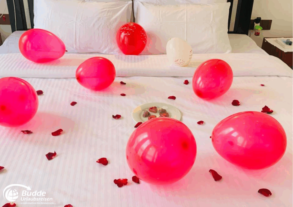 Rosa Luftballons und Rosenblätter auf einem Bett mit einem Teller voller Süßigkeiten. - buchbar im Reisebüro Budde Urlaubseisen