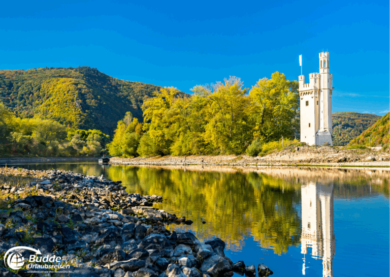Urlaub an der Nahe: Der Mäuseturm in Bingen am Rhein, umgeben von Wasser und Bäumen, reflektiert im ruhigen Wasser des Rheins. - buchbar im Reisebüro Budde Urlaubseisen