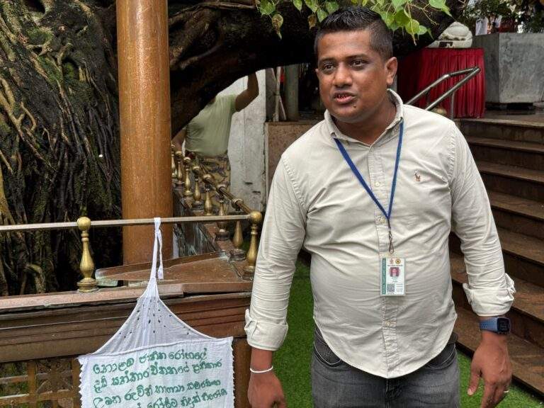 Mann in einem hellen Hemd steht neben einem Schild mit Informationen in Sinhala. - buchbar im Reisebüro Budde Urlaubseisen