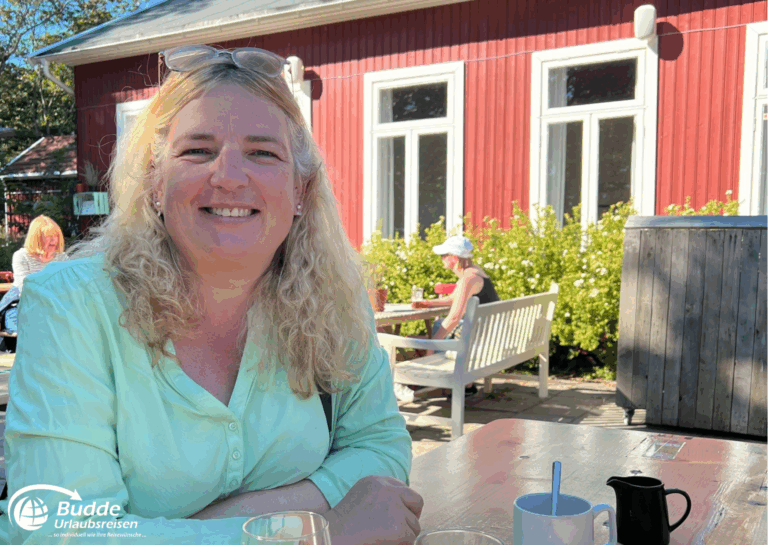 Norwegen Urlaub: Reiseexpertin Anke Budde und grünem Hemd sitzt an einem Tisch im Freien und lächelt. Norwegen Urlaub: Reiseexpertin Anke Budde und grünem Hemd sitzt an einem Tisch im Freien und lächelt.