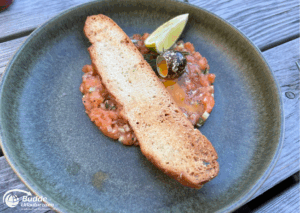 Norwegen Urlaub: Ein Teller mit Lachs-Tatar, einer Scheibe geröstetem Brot und einer Limettenscheibe.
