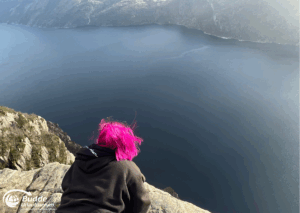 Norwegen Urlaub: Person mit pinken Haaren sitzt auf einem Felsen am Preikestolen mit Blick auf den Fjord.