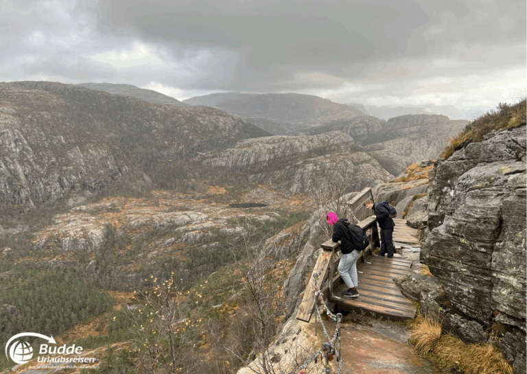 Norwegen Urlaub: Zwei Personen stehen auf einer Aussichtsplattform am Preikestolen mit Blick auf die umliegenden Berge. Norwegen Urlaub: Zwei Personen stehen auf einer Aussichtsplattform am Preikestolen mit Blick auf die umliegenden Berge.