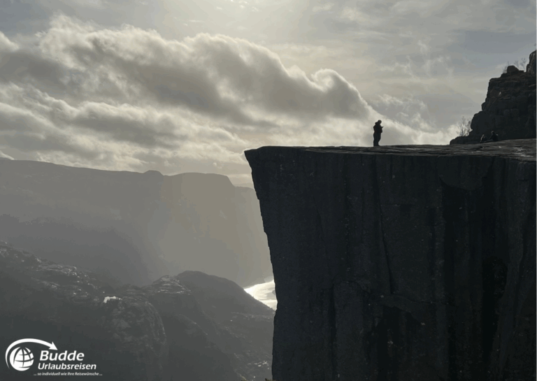 Norwegen Urlaub: Eine Person steht auf dem Preikestolen, einer steilen Klippe in Norwegen, mit Blick auf die umliegende Landschaft. Norwegen Urlaub: Eine Person steht auf dem Preikestolen, einer steilen Klippe in Norwegen, mit Blick auf die umliegende Landschaft.