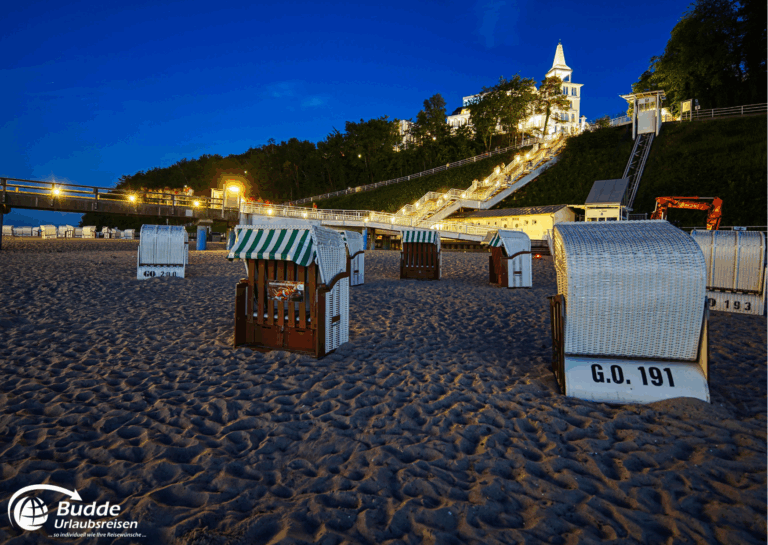 Ostseeurlaub Insel Rügen: Strandkörbe auf dem Sandstrand von Binz bei Nacht mit beleuchtetem Hintergrund.