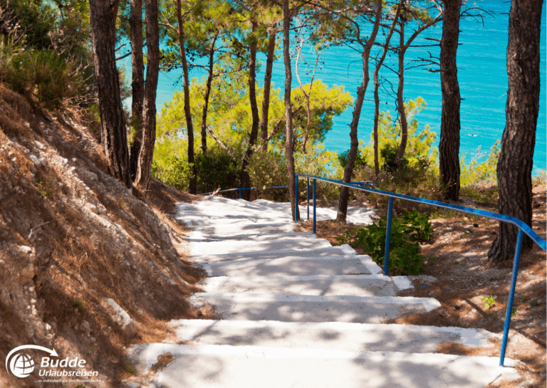 Samos traumhafte Kykladeninsel Griechenlands Betonstufen mit einem blauen Geländer, die einen Hang hinunterführen, umgeben von Bäumen und Wasser im Hintergrund.