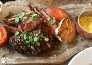 Urlaubsreisen nach London: Gegrilltes Steak auf einem Holzbrett mit Tomaten, Knoblauch und Sauce.