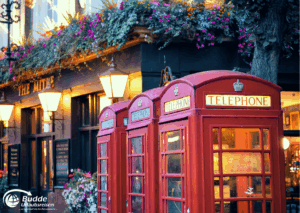 Urlaubsreisen nach London: Drei rote Telefonzellen mit dem Schriftzug 'TELEPHONE' in London, umgeben von Blumen und Laternen.