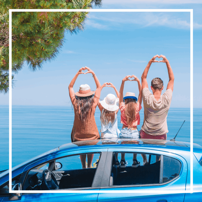 Vorteile von Pauschalreisen: Familie mit vier Personen, die auf dem Autodach eines blauen Autos am Meer sitzt und Herzformen mit den Händen macht.