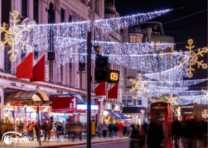 Weihnachtsshopping nach London: Weihnachtliche Lichter und Dekorationen über einer belebten Straße in London bei Nacht.