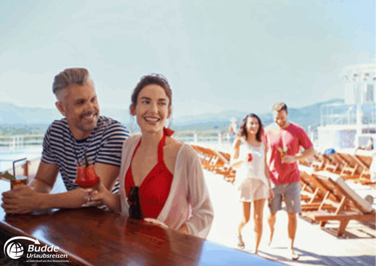 Weltreise Queen Mary 2: Ein Mann und eine Frau genießen Cocktails auf einem Schiff, während ein weiteres Paar im Hintergrund vorbeigeht.