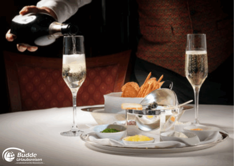 Weltreise Queen Mary 2: Ein Kellner schenkt Champagner in ein Glas, während Beilagen auf einem Tisch präsentiert werden.