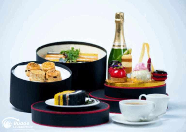 Weltreise Queen Mary 2: Ein Set mit verschiedenen Desserts, Champagner und einer Tasse Tee in eleganten Boxen.