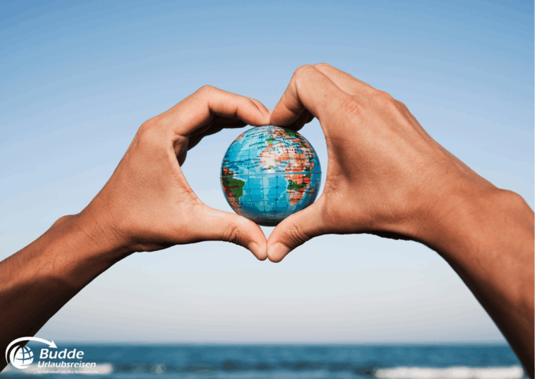 Weltreise Queen Mary 2: Hände, die ein Herz um eine kleine Erdkugel formen, vor einem blauen Himmel.