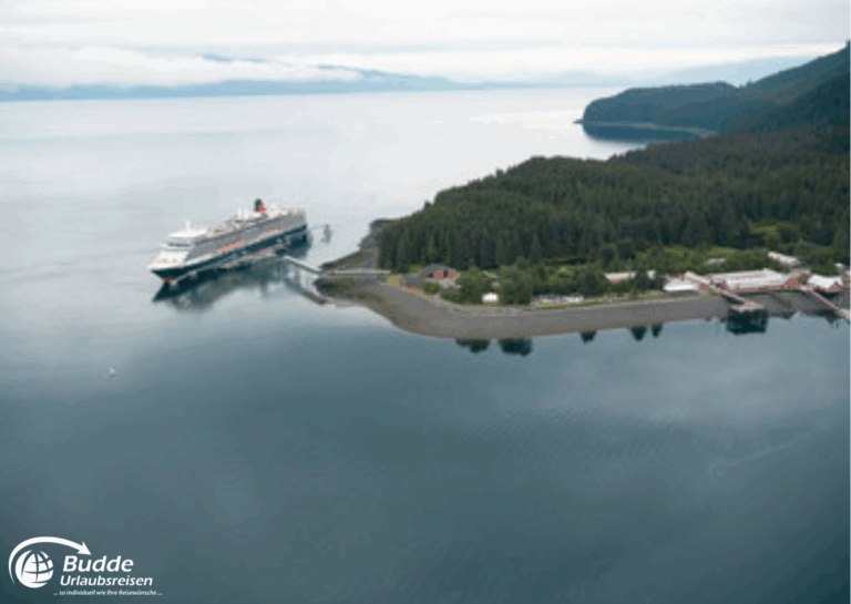 Weltreise Queen Mary 2: Ein Kreuzfahrtschiff liegt in ruhigem Wasser, umgeben von Wald und Küste.