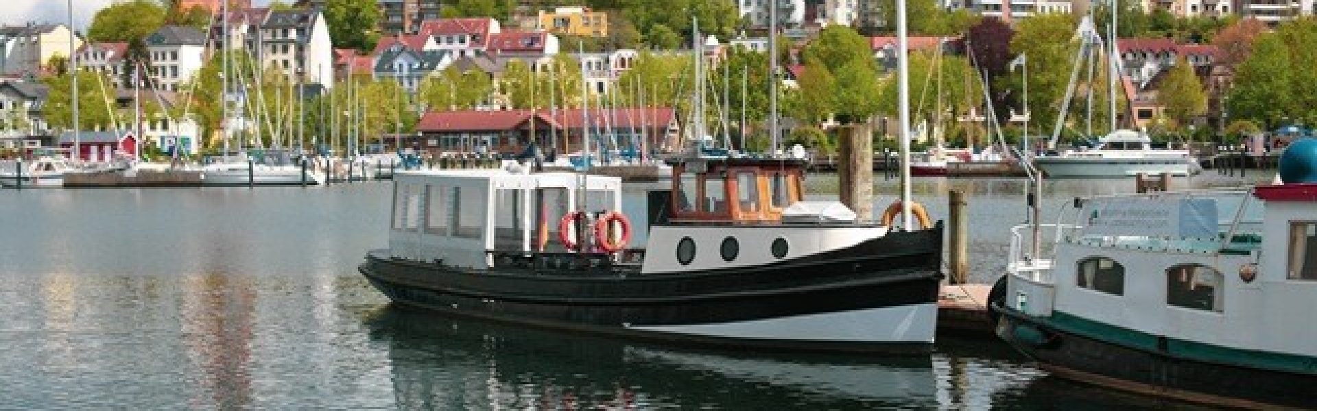 Barkasse Solitüde Schiff-Flensburg-Ostsee Ferienregion Das Bild zeigt die charmante Barkasse Solitüde, ein Schiff, das gemütliche Fahrten entlang der Ostseeküste in der Ferienregion Flensburg anbietet. Die Barkasse gleitet sanft über das ruhige Wasser und bietet den Passagieren eine entspannte Möglichkeit, die malerische Küstenlandschaft zu erkunden. Mit ihrem klassischen Design und ihrem freundlichen Personal ist die Solitüde ein beliebtes Schiff für Ausflüge und Entdeckungstouren. Auf dem Bild ist sie vor der Kulisse von Flensburg zu sehen, einer historischen Stadt, die für ihre maritimen Traditionen bekannt ist.