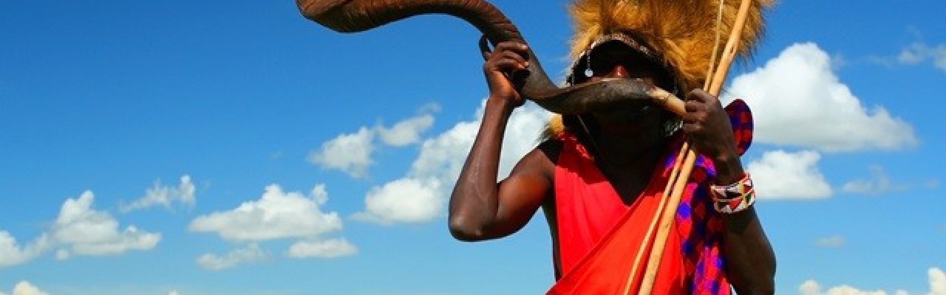 Massai-Krieger, der traditionelles Horn spielt. Afrika. Kenia. Masai Mara Das fesselnde Bild zeigt einen mutigen Massai-Krieger aus Kenia, der ein traditionelles Horn spielt. Die farbenfrohe Kleidung des Kriegers und seine stolze Haltung verleihen dem Bild eine authentische Atmosphäre. Das Horn, das er spielt, erzeugt einen kraftvollen Klang, der die Schönheit der afrikanischen Kultur widerspiegelt. Dieses Bild lädt den Betrachter ein, in die faszinierende Welt der Massai einzutauchen und die lebendige Kultur und Traditionen dieses faszinierenden Volkes zu entdecken. Erleben Sie die kraftvolle Energie und die fesselnde Musik der Massai-Krieger inmitten der atemberaubenden Landschaft der Masai Mara.